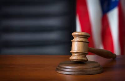 Wooden gavel laying on top of a wooden desk with an American flag blurred in the background