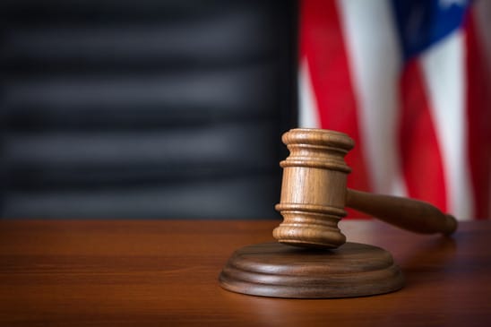 Wooden gavel laying on top of a wooden desk with an American flag blurred in the background