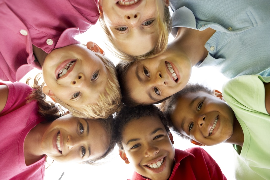 Six children gathered in a circle with their heads touching and looking down smiling at the camera