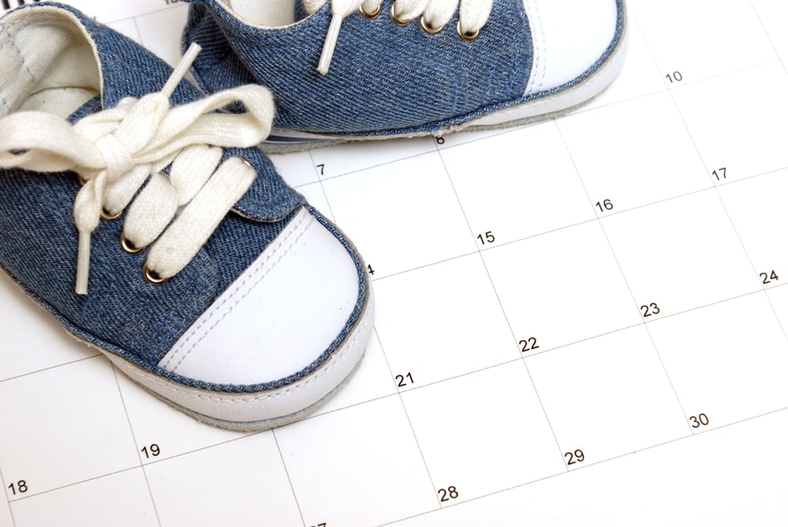 Blue denim baby shoes with white laces on top of a white calendar with black font