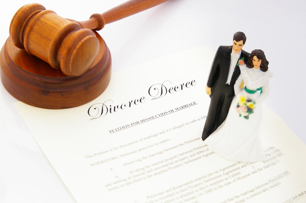 Divorce decree form with a wedding cake topper of a bride and groom standing on top next to a wooden gavel