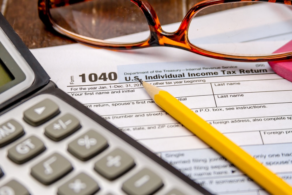 Form 1040 U.S. Individual income tax return with a yellow number 2 pencil, calculator, and a red pair of glasses arranged on top of the form